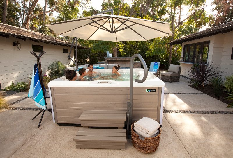 Family relaxing in a Hot Spring Limelight hot tub under a patio umbrella